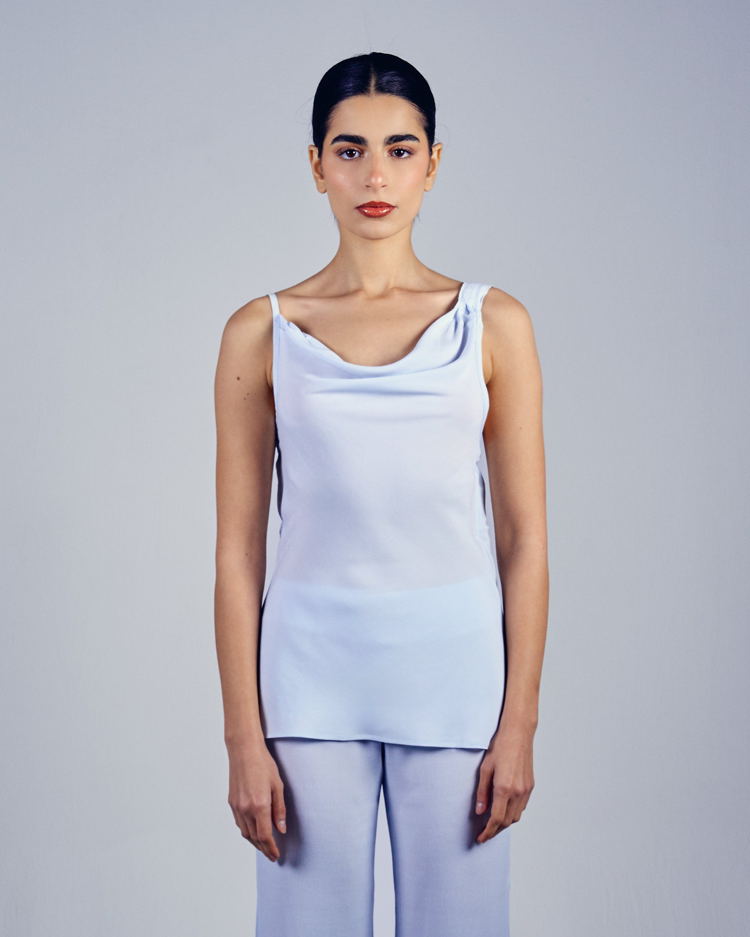 Woman wearing a light blue sleeveless top and wide-leg pants against a plain background